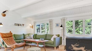 Ein gemütliches Wohnzimmer mit einem grünen Sofa, einem Holzsesseln, einem gestreiften Hocker und einer schwarzen Kommode mit einem Bild von einem Hirsch.