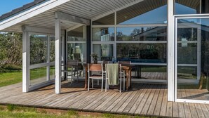 Une terrasse extérieure moderne avec des murs en verre, des meubles en bois et une vue dégagée sur le paysage environnant.