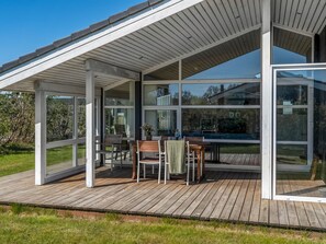Une terrasse extérieure moderne avec des murs en verre, des meubles en bois et une vue dégagée sur le paysage environnant.