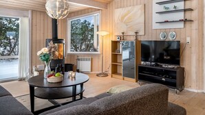 Un salon moderne doté d’une cheminée, d’un téléviseur et d’une grande fenêtre donnant sur un paysage arboré.