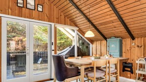L'interno di una baita in legno con un tavolo da pranzo, sedie, un armadietto blu e vista all'esterno.