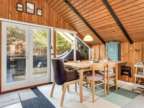 Ein Holzblockhaus-Innenraum mit Esstisch, Stühlen, einem blauen Schrank und Blick ins Freie.