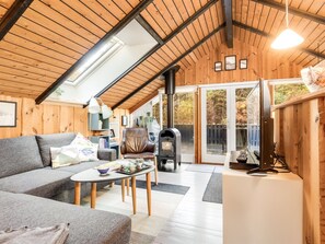 Ein gemütliches Blockhauss-Interieur mit Holzbalkendecke, einer Couch, einem Tisch und einem Kamin.