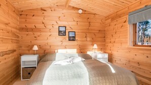Camera da letto in una baita di legno, con un letto, due comodini, una finestra e due quadri appesi alla parete.