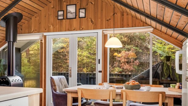 Una cucina accogliente con stufa a legna, un'area pranzo con sedie e tavolo, e ampie finestre con vista sugli alberi.