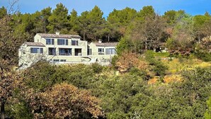 A two-story house with a stone facade, surrounded by dense trees and shrubs. - Mas La Rose Sauvage – Elegant Stone Villa with Panoramic Views near Gordes (Murs)