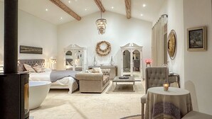 A spacious bedroom with a large bed, a sitting area with a coffee table, and a separate bathroom with a bathtub. - Mas La Rose Sauvage – Elegant Stone Villa with Panoramic Views near Gordes (Murs)