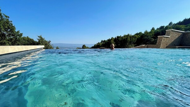 A clear blue pool with a stone wall on one side and a concrete edge on the other. - Mas La Rose Sauvage – Elegant Stone Villa with Panoramic Views near Gordes (Murs)