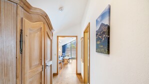 Um corredor com portas de madeira, vista para um quarto com uma mesa e cadeiras, e um quadro na parede.