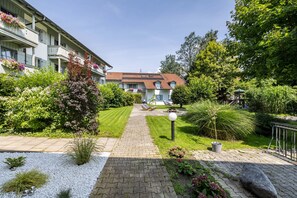 En gårdsplads med en belagt sti, et lille haveområde med planter og blomster, samt en bygning med altaner.