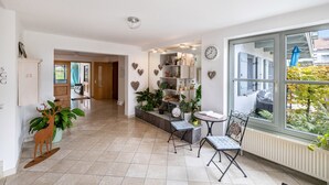 Um corredor amplo com área de jantar, plantas em vasos e vista para o exterior.