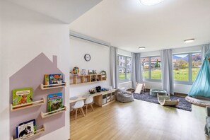 Et børneværelse med et skrivebord, reoler med bøger, en poseleje og udsigt til et grønt landskab.