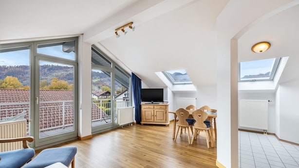 Um quarto espaçoso com uma grande porta de vidro deslizante, área de refeições com mesa e cadeiras, televisão e um claraboia.