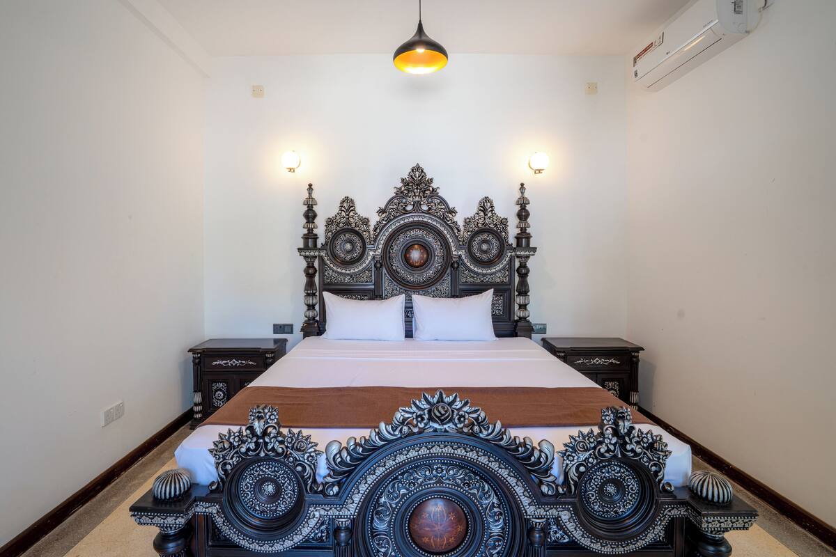 Una cama bien hecha con un cabecero ornamentado, dos mesitas de noche y una lámpara colgante.