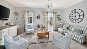 Een woonkamer met een bank, fauteuils, een salontafel, een televisie, een boekenkast en een grote wandklok.