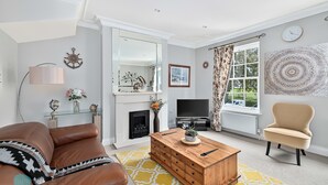 Een woonkamer met een bruine leren bank, een houten salontafel, een beige fauteuil, een televisie en een open haard.