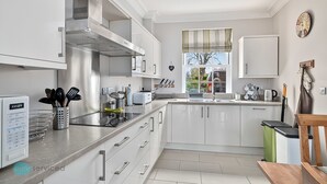 Een moderne keuken met witte kastjes, roestvrijstalen apparatuur en een raam met gordijnen.