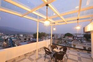 A balcony with a glass roof, wicker chairs, and a table. - Ganga Inn By YatriMap (Rishikesh)
