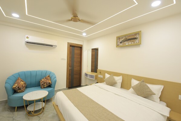 A hotel room with a bed, a blue sofa, a small round table, and an air conditioning unit. - Ganga Inn By YatriMap (Rishikesh)
