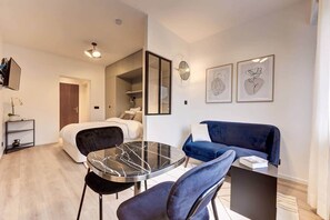 Habitació moderna i ben il·luminada amb un llit, un sofà blau, una taula rodona amb cadires i obra d'art a les parets.