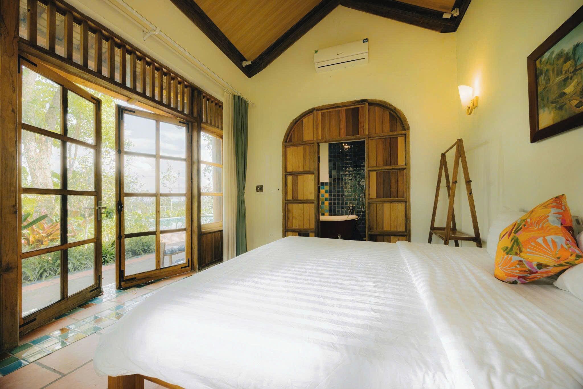Une chambre avec un grand lit, une fenêtre en arc de cercle en bois et une vue sur l’extérieur.