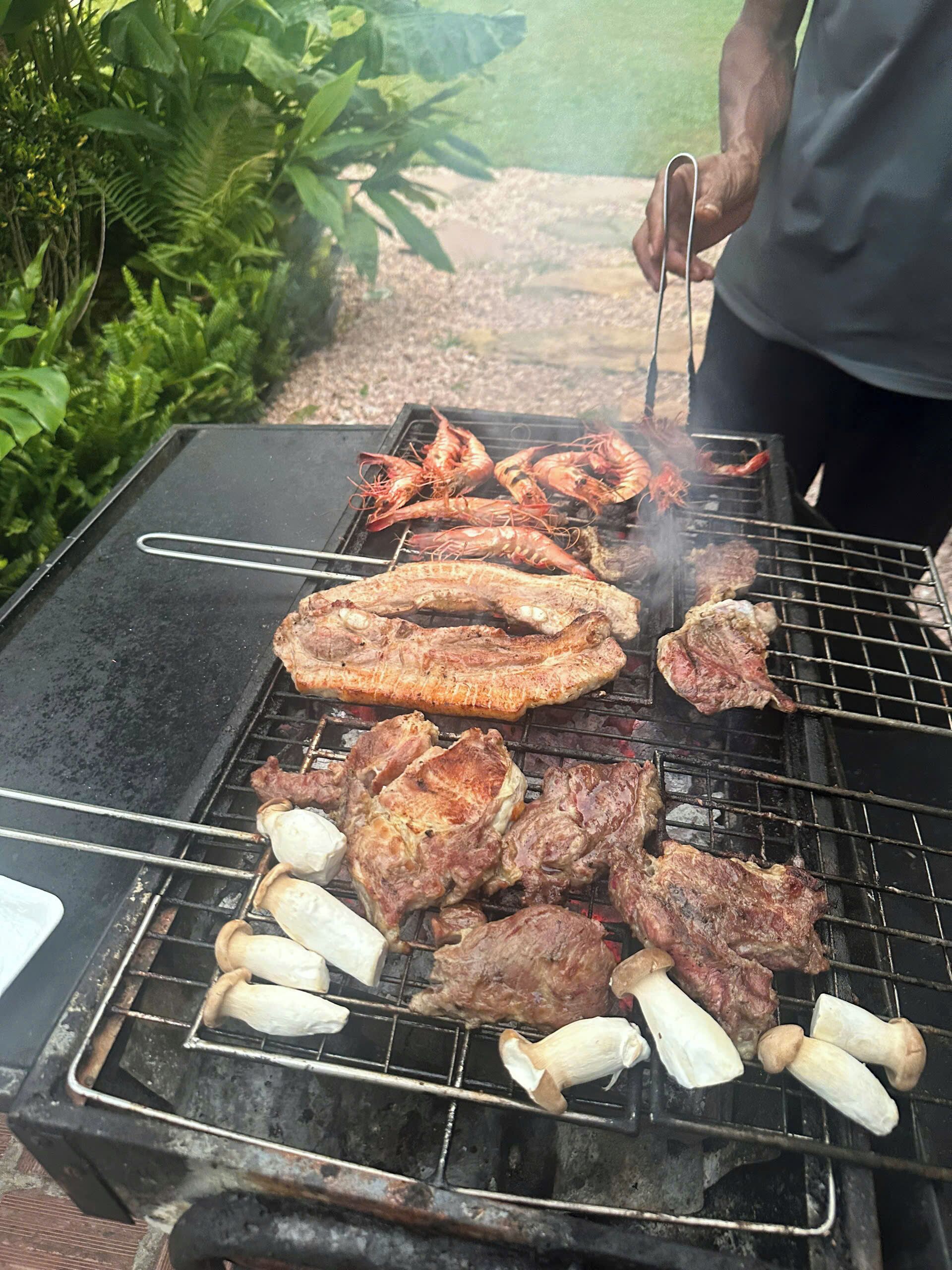 A grill with various meats and shrimp being cooked outdoors.