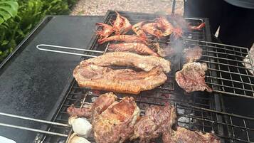 A grill with various meats and shrimp being cooked outdoors.