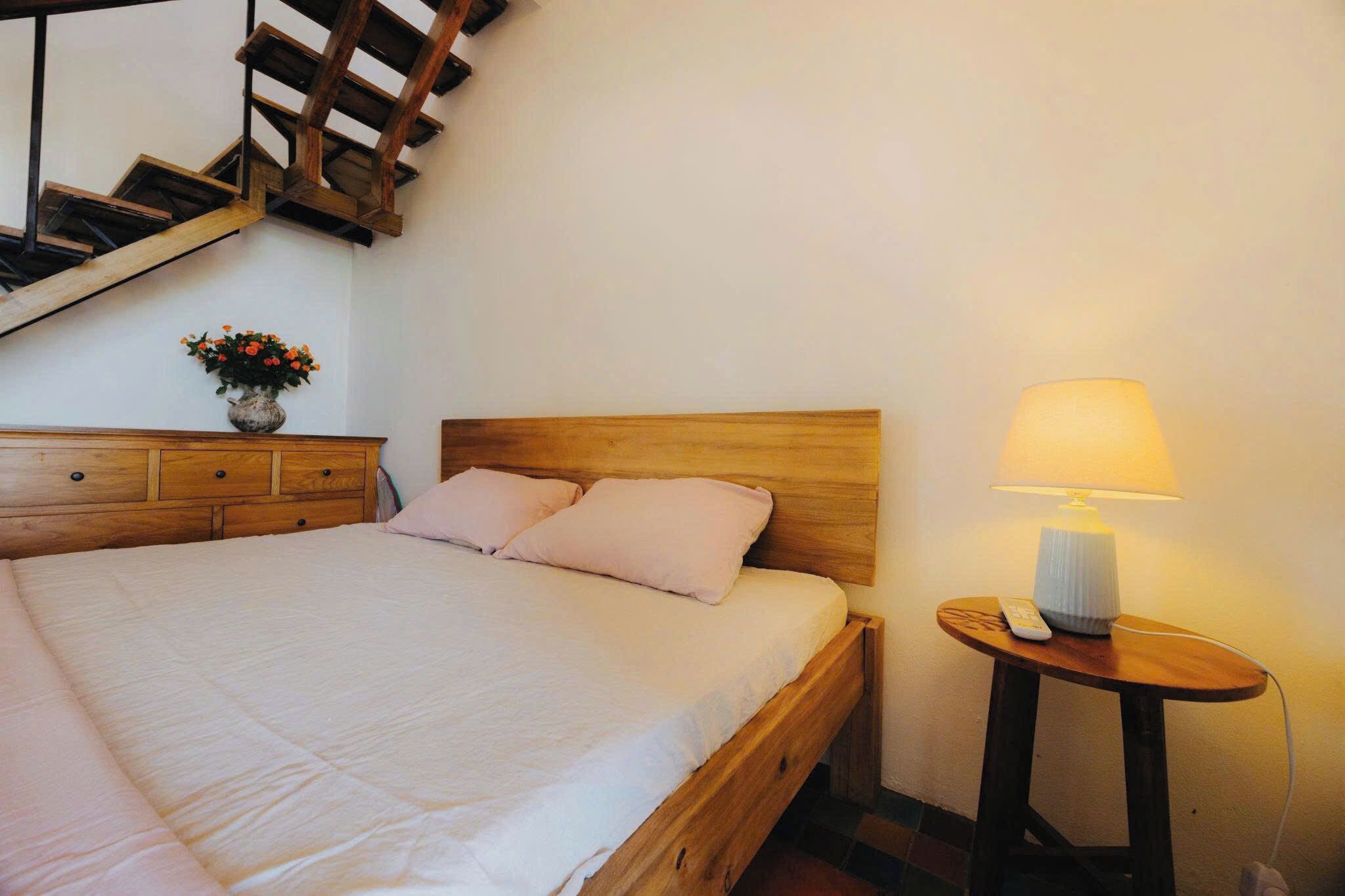 Una camera da letto con un letto in legno, un comodino con una lampada e un vaso con fiori su un mobiletto.