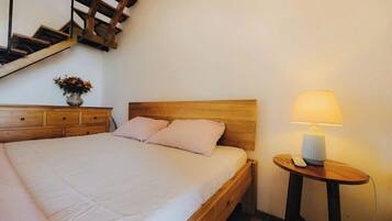 Una camera da letto con un letto in legno, un comodino con una lampada e un vaso con fiori su un mobiletto.