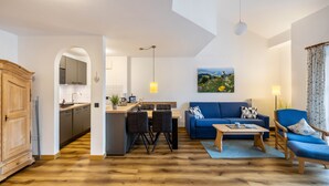 A modern living room with a blue sofa, a coffee table, and a dining area with a kitchen in the background. - Apartment 'Fewo Brünnstein - Zimmer 50' with Mountain View, Shared Garden & Wi-Fi (Oberaudorf)