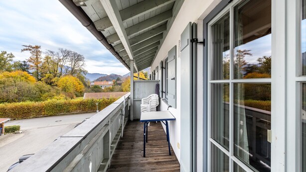A balcony with a table and chairs, overlooking a landscaped area with trees and mountains. - Apartment 'Fewo Brünnstein - Zimmer 50' with Mountain View, Shared Garden & Wi-Fi (Oberaudorf)