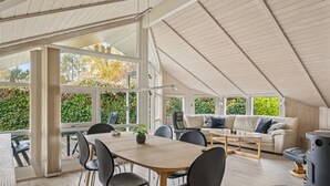 Un soggiorno e zona pranzo open space con soffitto alto, ampie finestre e vista sul verde.