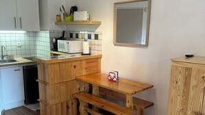 A compact kitchen with wooden cabinets, a built-in microwave, and a wooden table. - South-facing studio with direct runway access sleeps 4 Vallée Blanche residence (Allos)