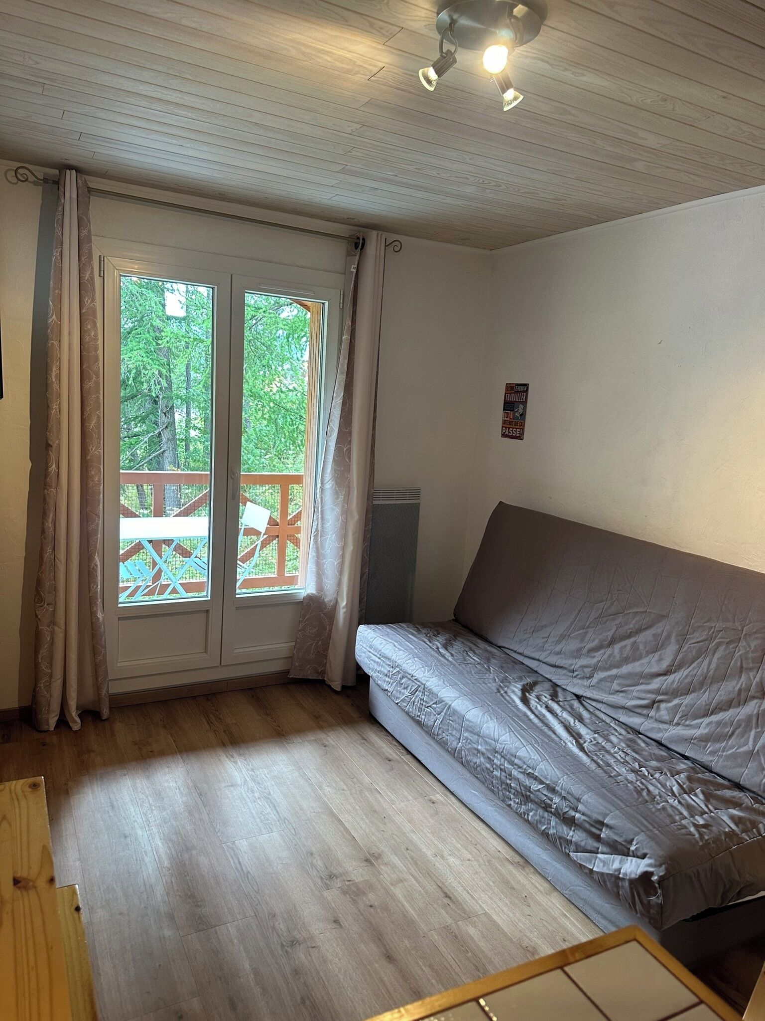A room with a wooden floor, a grey sofa, a window with curtains, and a ceiling fan.