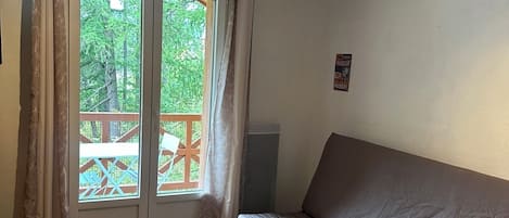 A room with a wooden floor, a grey sofa, a window with curtains, and a ceiling fan.