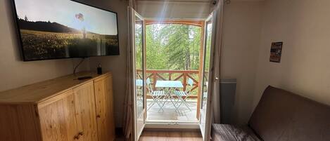 Una habitación con un armario de madera, un televisor en la pared, una cama y un balcón con una mesa y sillas.