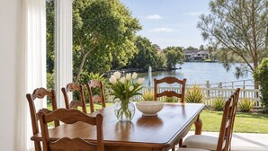 Une table à manger avec des chaises, un vase rempli de fleurs et une vue sur un lac bordé d’arbres et de maisons.