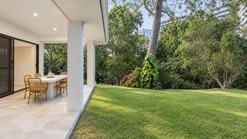 Eine moderne Terrassengruppe im Freien mit Esstisch und Stühlen, umgeben von einem gepflegten Rasen und Bäumen.