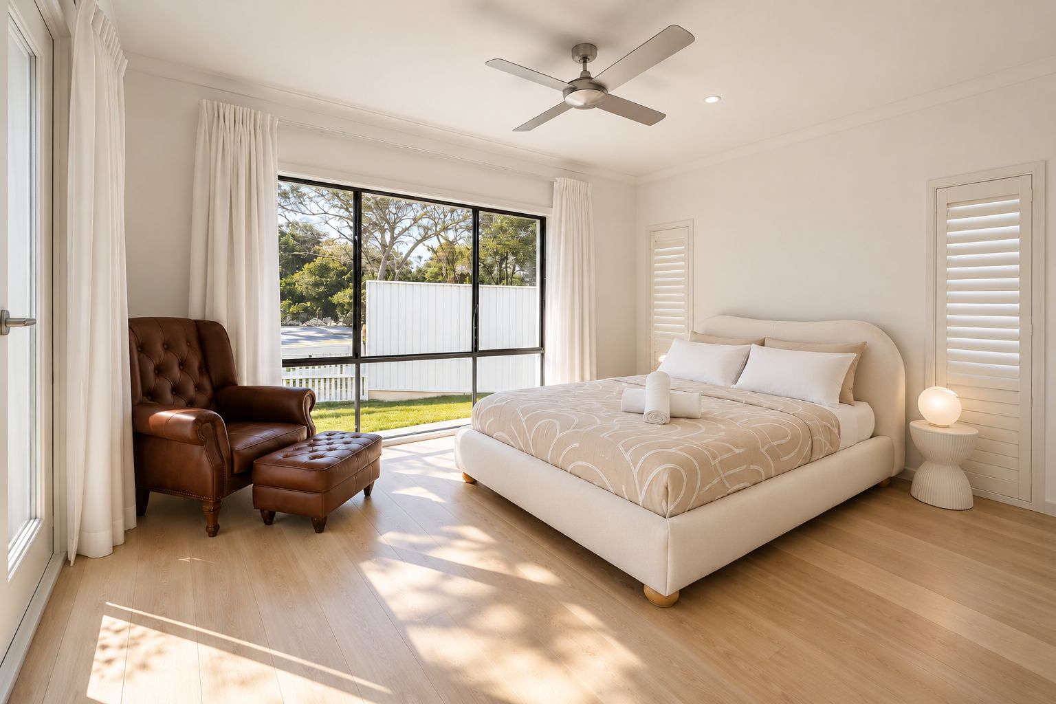 Ein Schlafzimmer mit einem großen Bett, einem Sessel, einem Deckenventilator und einem Fenster mit Blick auf Bäume.