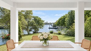 Un espace repas offrant une vue sur un lac et la verdure, avec une table blanche et des chaises en osier.