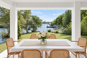 A dining area with a view of a lake and greenery, featuring a white table and wicker chairs. - Creekside Manor - Spacious | Nature & Serenity (Biggera Waters)