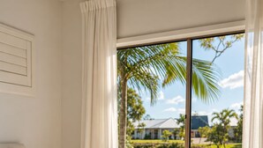 Une chambre d’hôtel avec un grand lit, une vue sur un plan d’eau et un palmier devant la fenêtre.