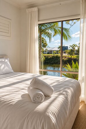 A hotel room with a large bed, a view of a body of water, and a palm tree outside the window. - Creekside Manor - Spacious | Nature & Serenity (Biggera Waters)
