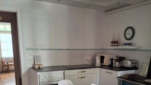 Un comedor con una mesa preparada para dos, una cocina con electrodomésticos y un reloj en la pared.