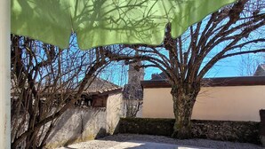 Un área de comedor al aire libre con una mesa preparada para dos, una sombrilla verde y vistas a un muro de piedra y árboles.