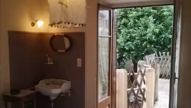 Un dormitorio con cama, mesita de noche, lámpara colgante, ventana con vistas a la vegetación y puerta que da al exterior.