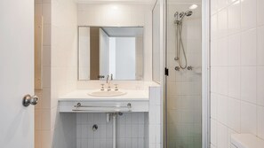 A modern bathroom with a white sink, mirror, and glass-enclosed shower.