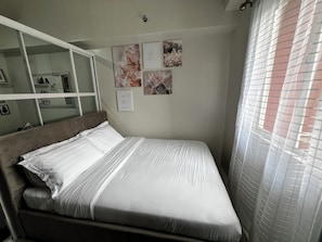 A neatly made bed with white linens, a headboard, and a wall with framed artwork.