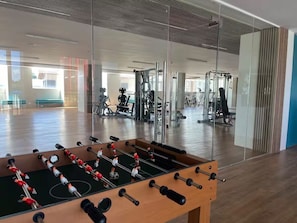 A gym with a foosball table, exercise equipment, and a large mirror reflecting the space.