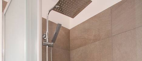 A walk-in shower with a glass door and a showerhead mounted on a wall.